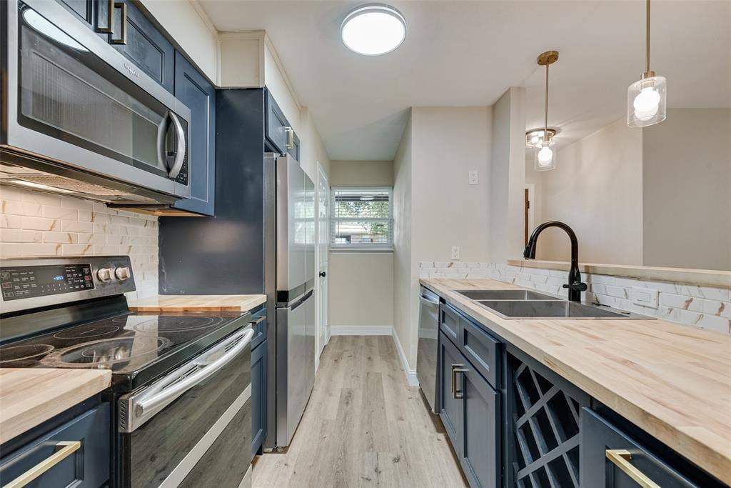1238 Neptune Drive, Cedar Hill, TX 75104 Kitchen featuring navy cabinetry, butcher block countertops, stainless steel appliances, a white brick-pattern backsplash, and built-in wine storage