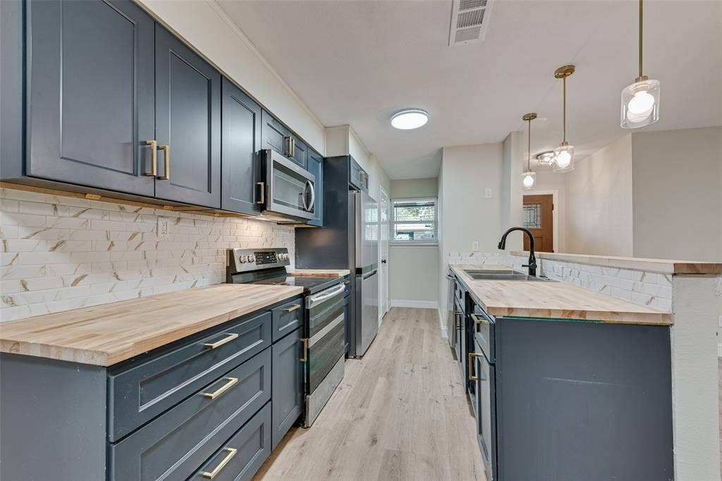 1238 Neptune Drive, Cedar Hill, TX 75104 Kitchen featuring dark blue cabinetry with brass-finish hardware, wood-surface countertops, subway tile backsplash, stainless steel appliances, and wood-finish flooring