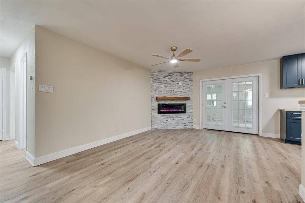 1238 Neptune Drive, Cedar Hill, TX 75104 Living space featuring wood-finish flooring, corner fireplace with stacked-stone masonry, natural wood mantel, and French doors