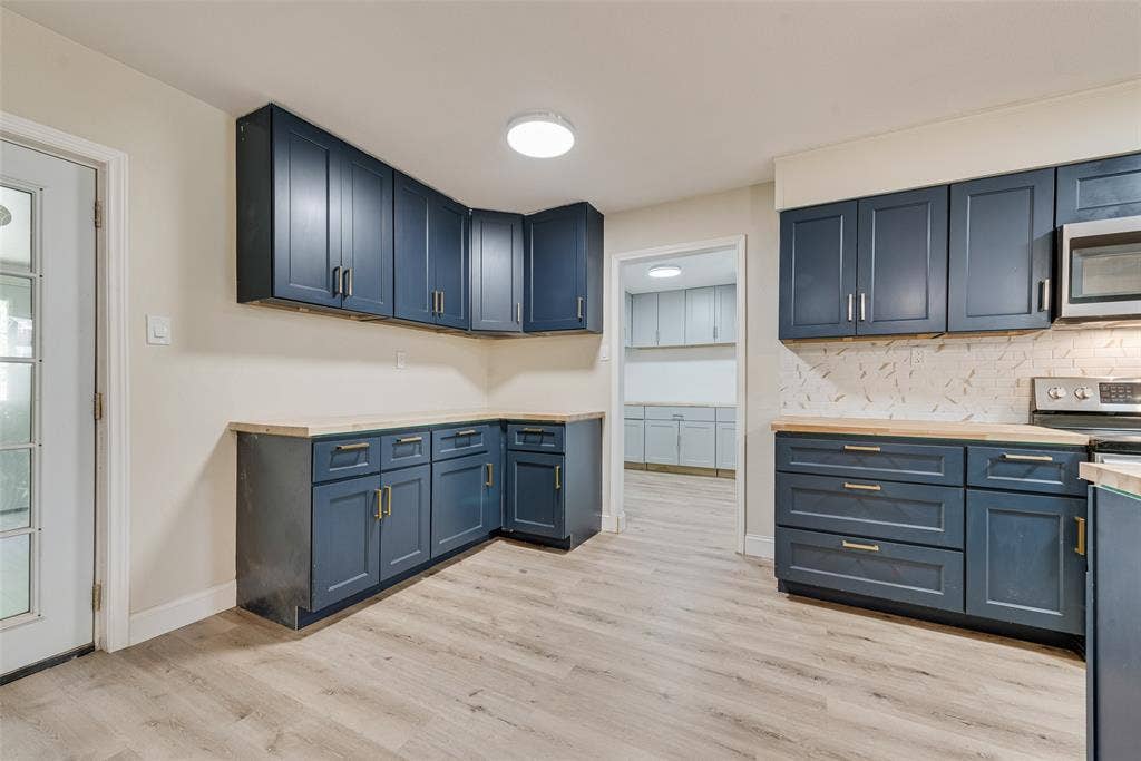 1238 Neptune Drive, Cedar Hill, TX 75104 Kitchen featuring navy blue cabinetry, light-toned wood-finish countertops, patterned tile backsplash, stainless steel appliances, and wood-finish flooring