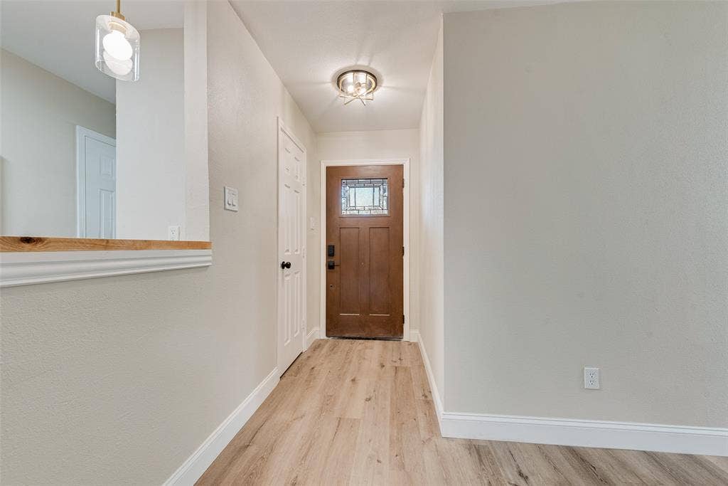 1238 Neptune Drive, Cedar Hill, TX 75104 Entryway featuring a wood-finish front door with a decorative glass insert, wood-finish flooring, a pass-through wall opening with a natural wood ledge, and dual overhead light fixtures