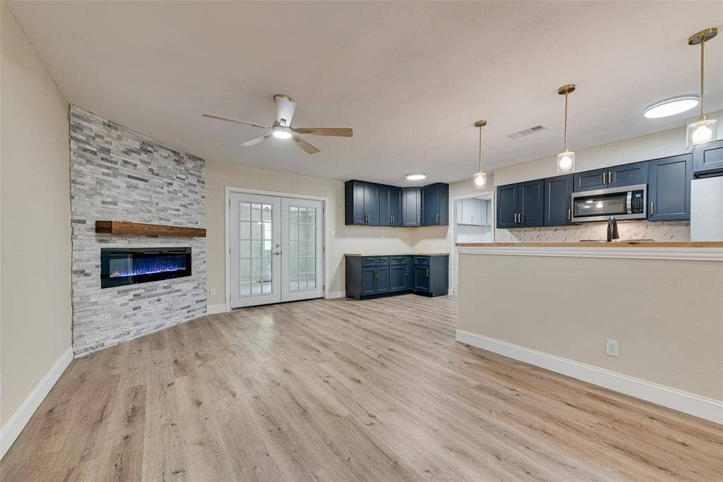 1238 Neptune Drive, Cedar Hill, TX 75104 Stone-accented fireplace with a wood mantel, navy blue cabinetry, wood-finish flooring, glass-paned double doors, and pendant lighting
