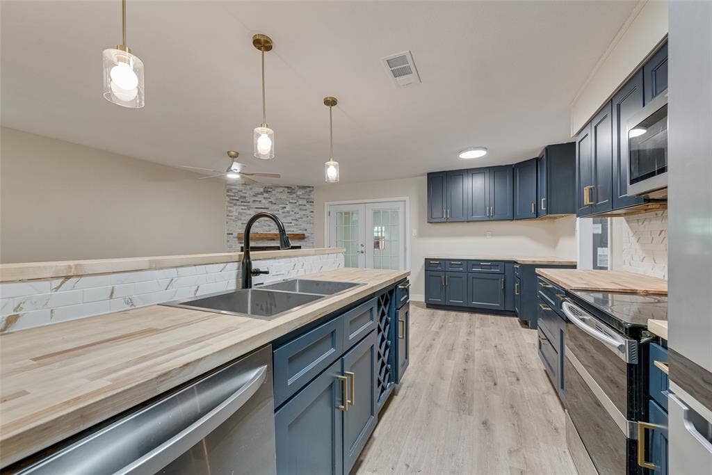 1238 Neptune Drive, Cedar Hill, TX 75104 Kitchen featuring navy cabinetry, butcher block countertops, white herringbone backsplash, wood-finish flooring, and three glass pendant lights
