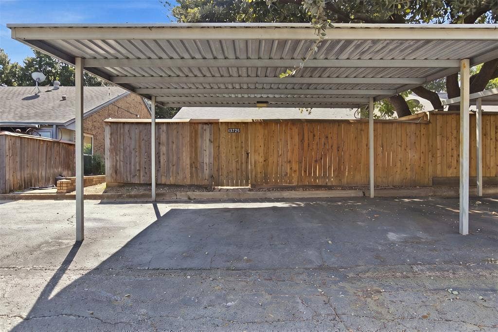 Covered carport featuring a metal roof, support columns, and vertical wood privacy fencing