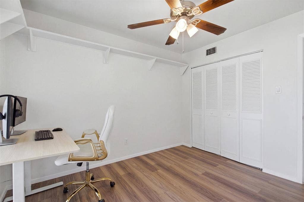 Room featuring wood-finish flooring, white louvered-door closet, ceiling fan with light fixture, and wall-mounted shelving