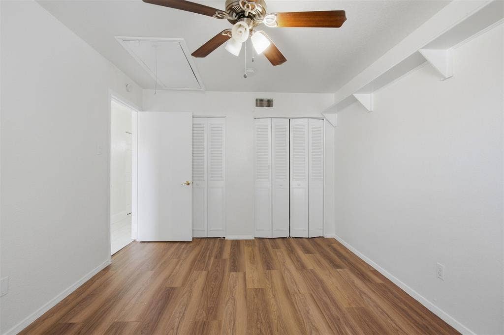 Interior space featuring wood-finish flooring, white louvered-door closets, ceiling fan with light fixture, and wall-mounted shelving