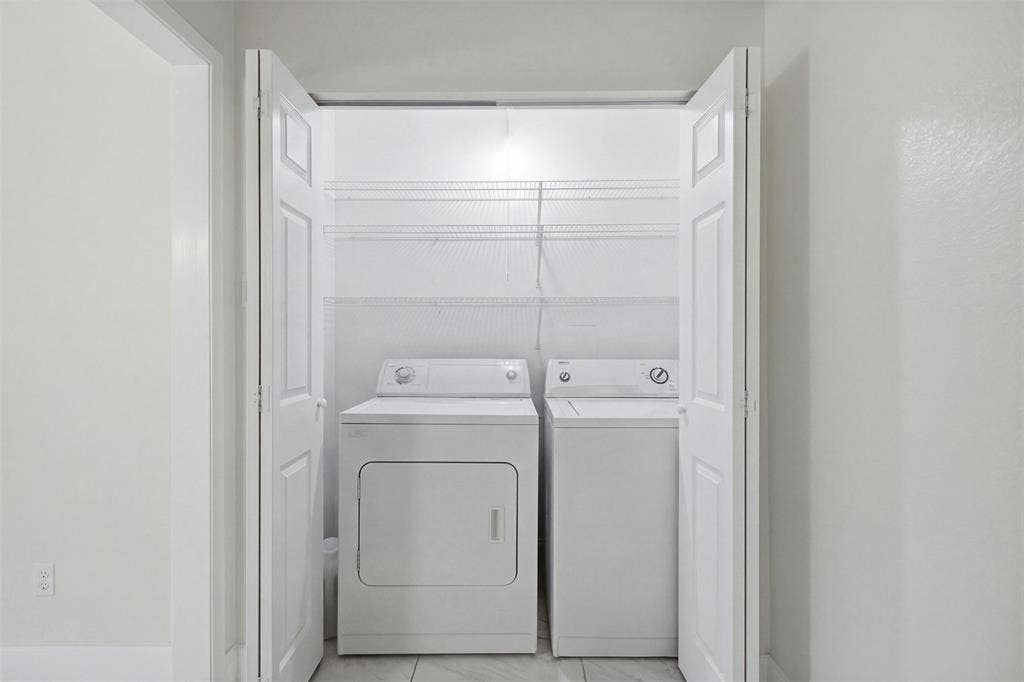Laundry closet featuring white bi-fold doors, white top-load appliances, and tiered wire shelving