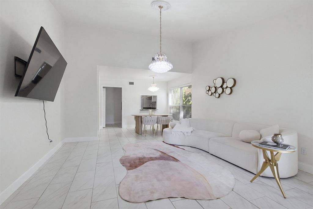 High-ceiling living area featuring large-format tile flooring, a multi-tiered crystal chandelier, and a secondary pendant light fixture