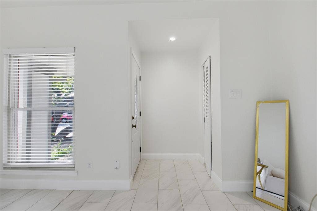 Interior space featuring tile flooring with a neutral-tone finish, single-hung window with horizontal blinds, recessed ceiling lighting, and a louvered bi-fold closet door