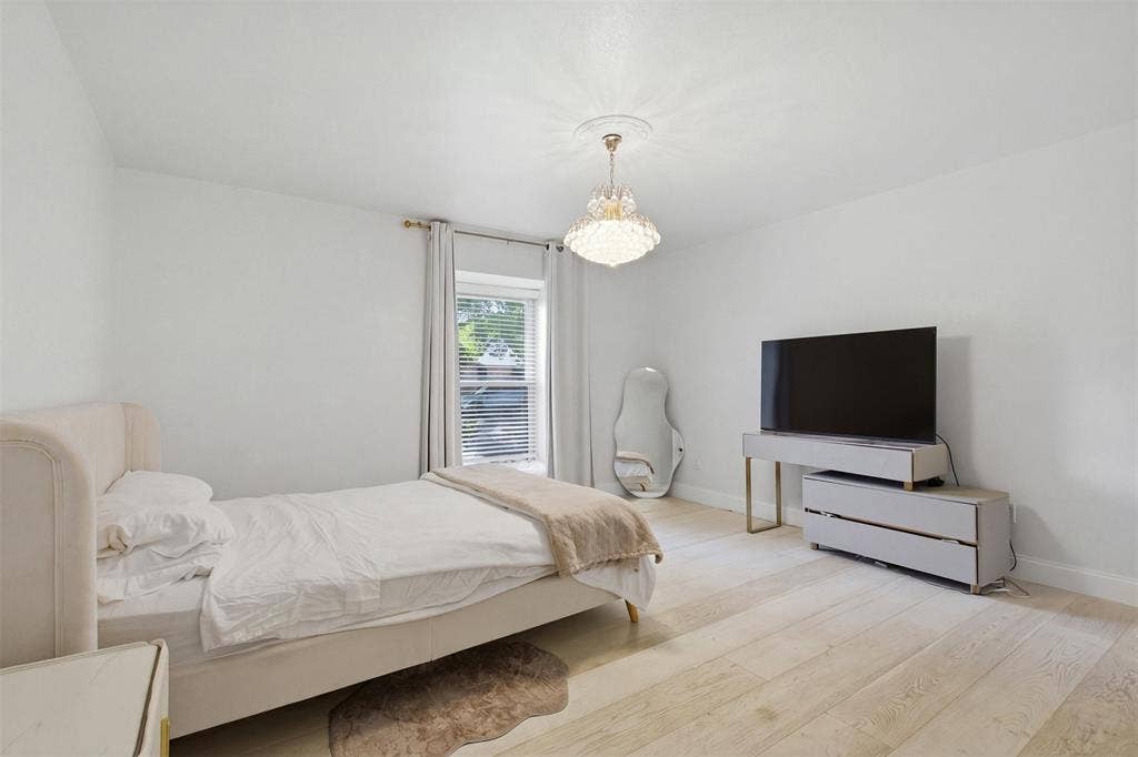 Neutral-toned wood-finish flooring, crystal-style chandelier with ceiling medallion, and white window casing