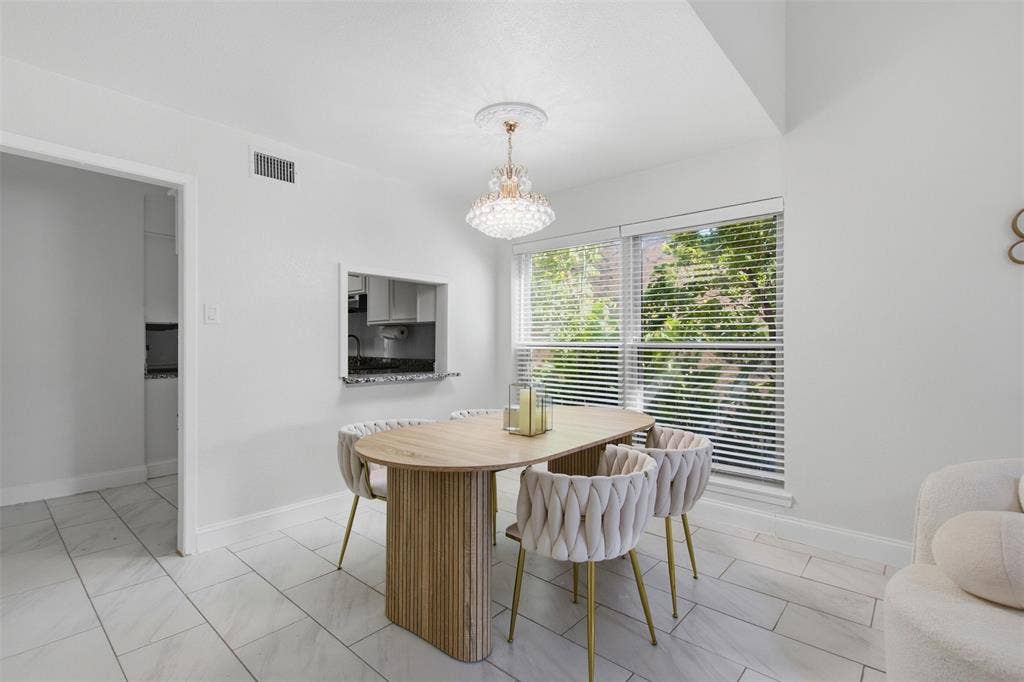 Dining area featuring large-format tile flooring, a decorative crystal chandelier, and a pass-through window with a stone-finish ledge