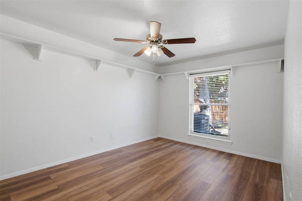 Wood-finish flooring, ceiling-mounted light fixture with fan, wall-mounted shelving, and window with horizontal blinds