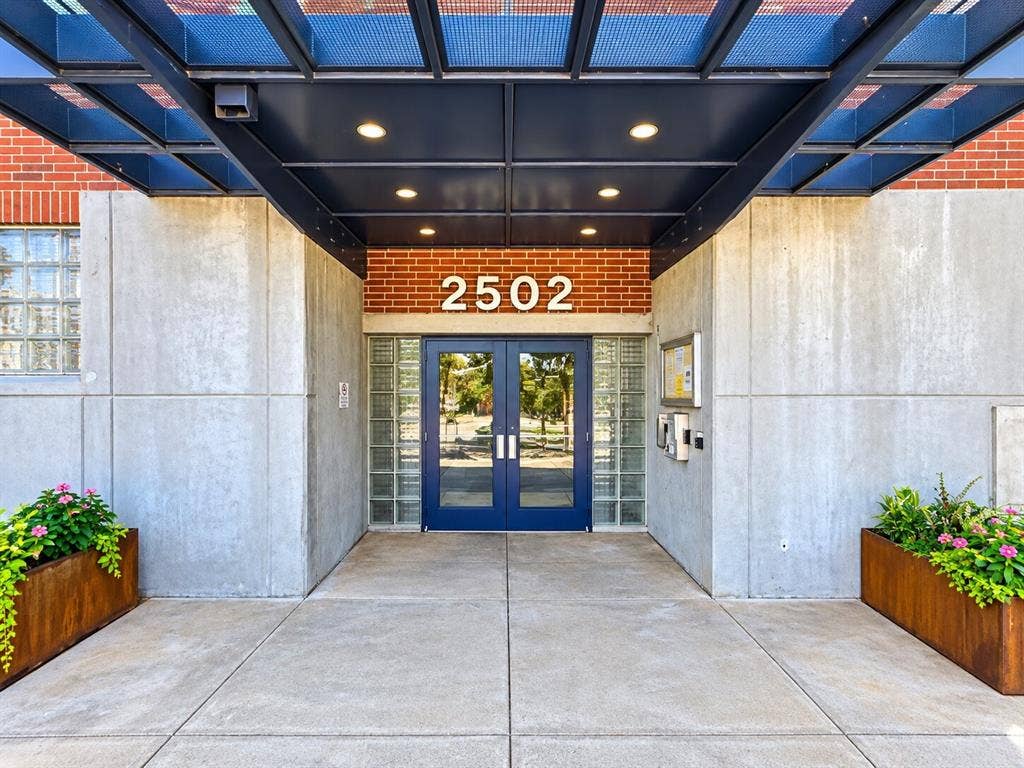 2502 Live Oak Street, #110, Dallas, TX 75204 Industrial-style entryway featuring exposed brick masonry, smooth concrete panels, a structural metal portico, glass block sidelights, and double doors with blue metal frames