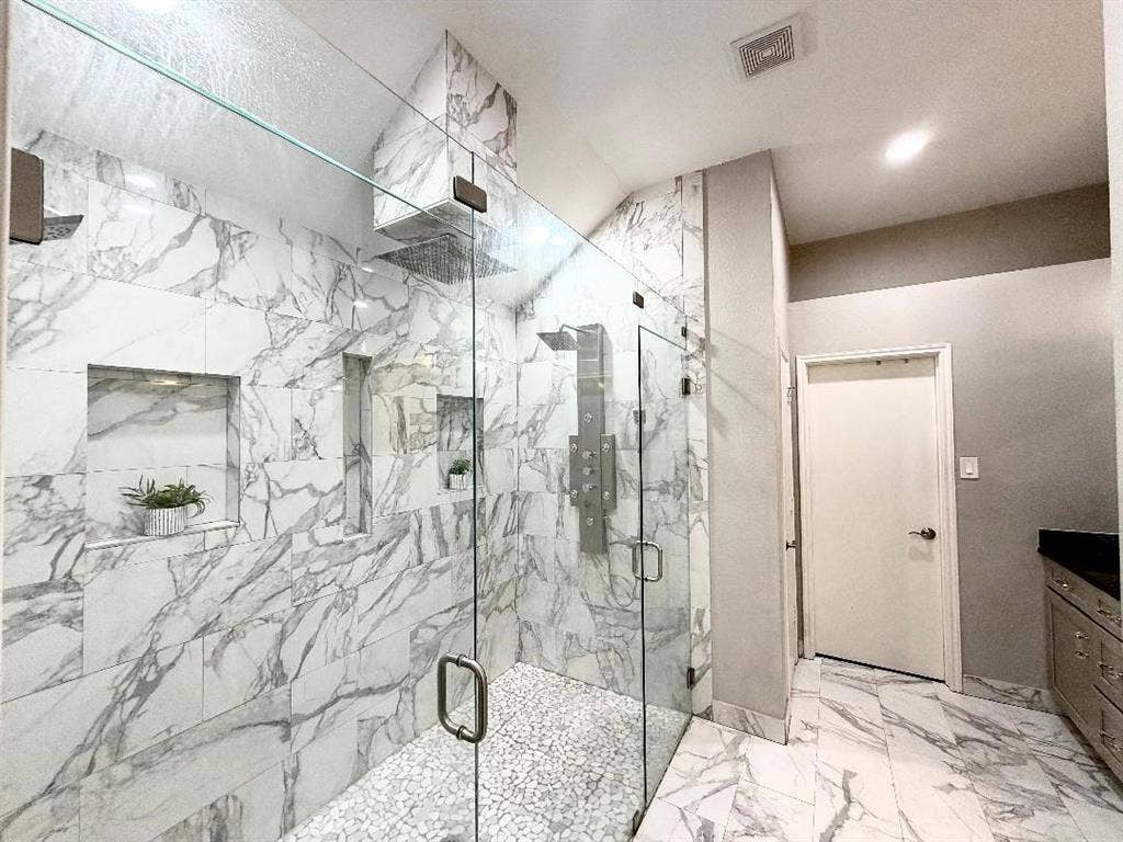 Walk-in shower featuring large-format stone-finish tile surround, pebble-texture flooring, frameless glass enclosure, multiple built-in shower niches, and an integrated multi-head shower system