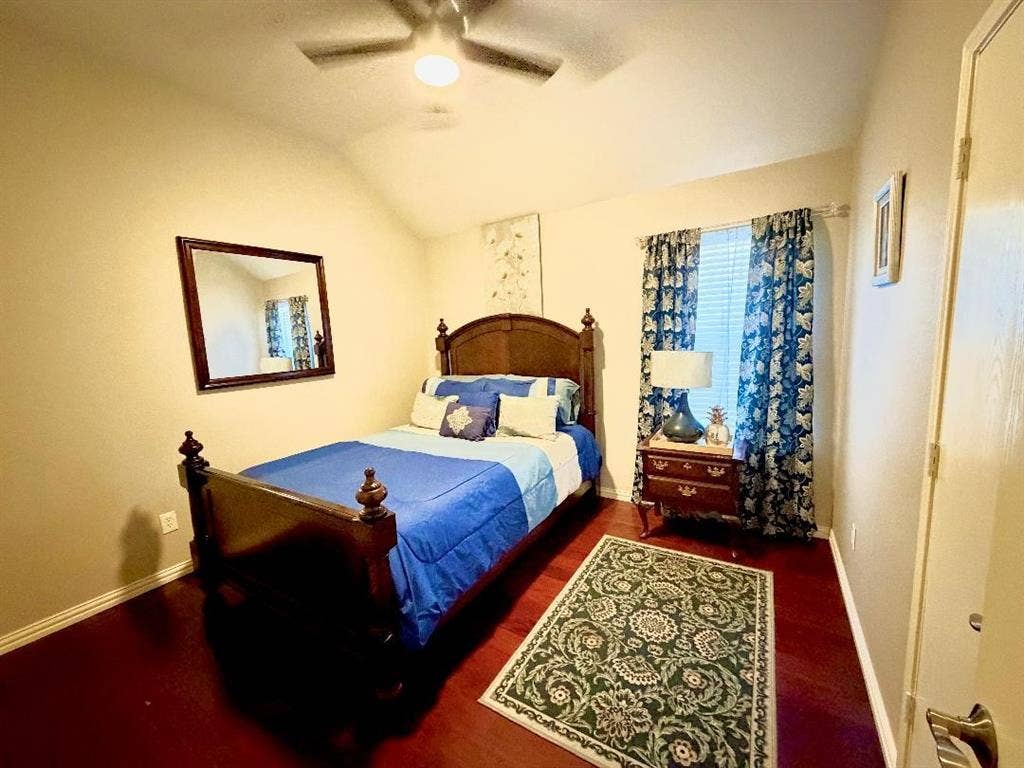 Vaulted ceiling featuring a central ceiling fan, wood-finish flooring, and a single window with curtain rod hardware