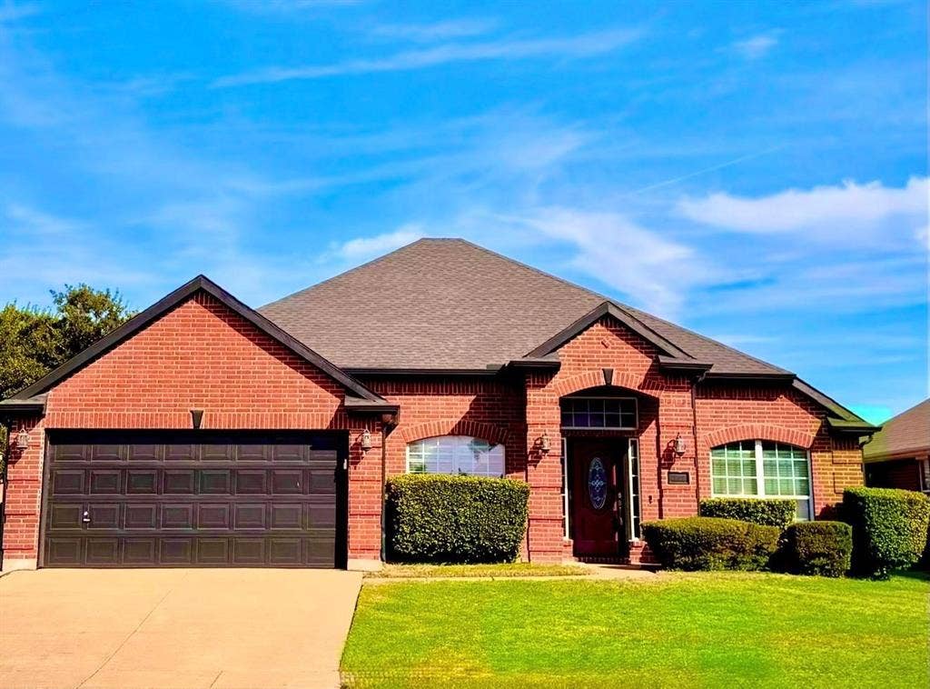 Single-story residence featuring a full red brick facade, arched window detailing, an asphalt shingle roof, and an attached two-car garage