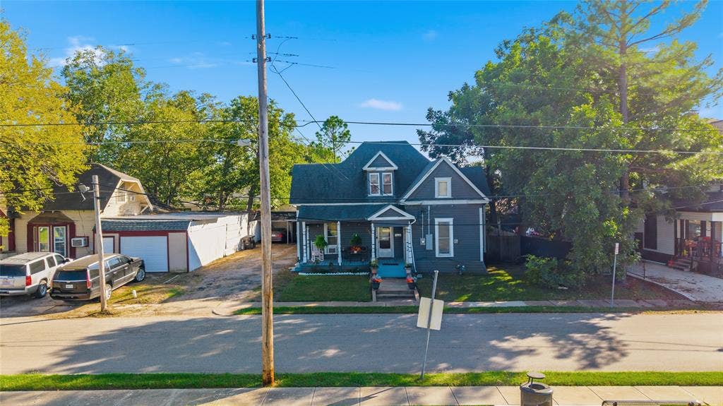 2309 Jones Street, Greenville, TX 75401 Two-story residence featuring a dark-toned facade, a steep-pitched gable roof, a covered front porch with decorative trim, and a detached structure with a white garage door