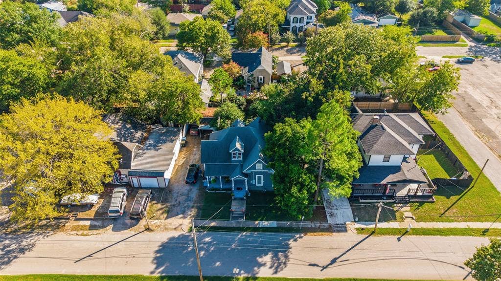 2309 Jones Street, Greenville, TX 75401 Aerial view featuring mature canopy trees, detached garage structure, asphalt-shingled roof, and paved driveway