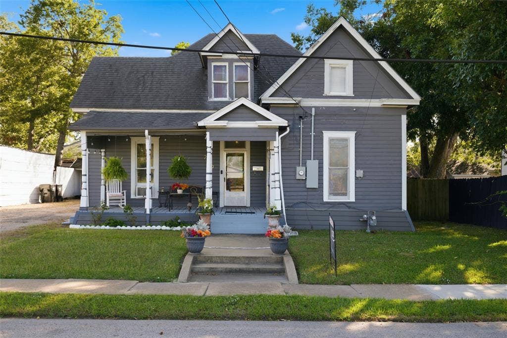 2309 Jones Street, Greenville, TX 75401 Victorian-style exterior featuring gray horizontal siding, a covered front porch, dual-gabled roofline, and concrete front steps