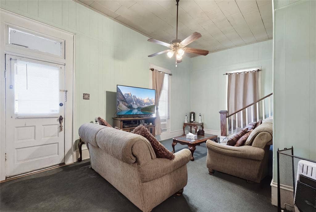2309 Jones Street, Greenville, TX 75401 Plank-paneled walls, ceiling featuring exposed wood-plank detailing, central ceiling fan with multi-bulb light fixture, multi-pane entry door with transom window, and staircase with wooden handrail