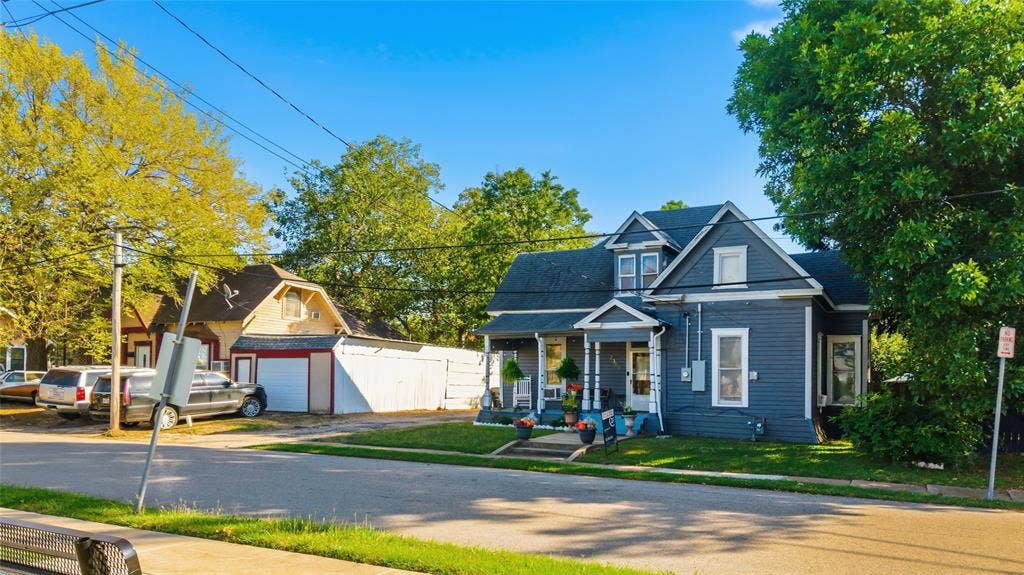 2309 Jones Street, Greenville, TX 75401 Two-story residence featuring horizontal lap siding, a covered front porch with decorative posts, a cross-gabled roofline, and a detached garage