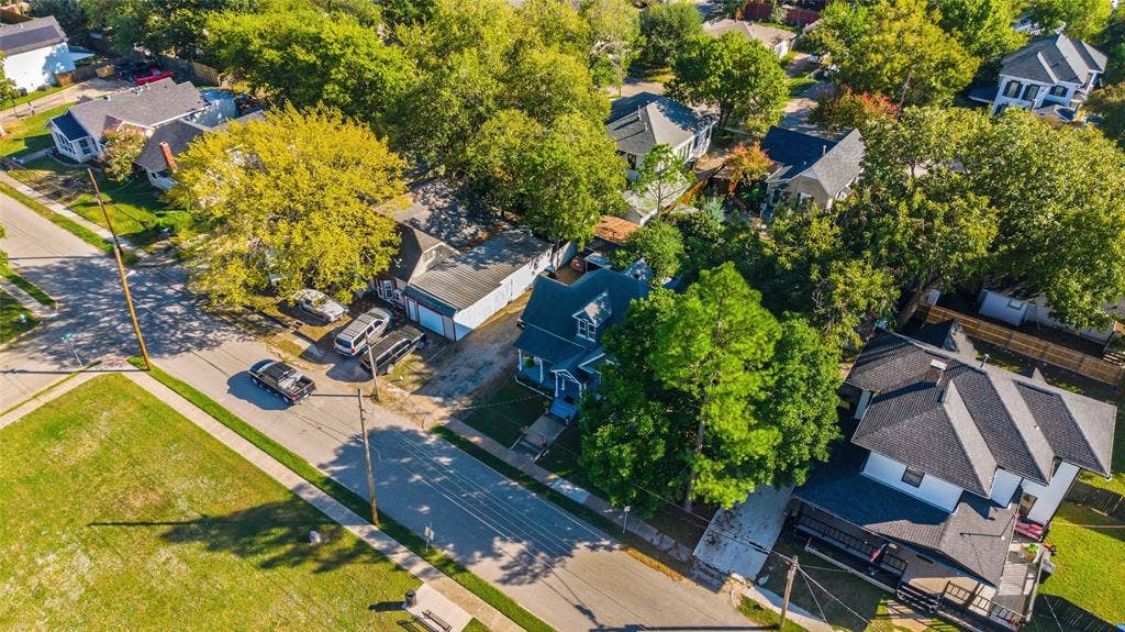 2309 Jones Street, Greenville, TX 75401 Aerial perspective featuring a multi-story residence with a pitched shingle roof, paved driveway, detached garage structure, and established trees throughout the lot