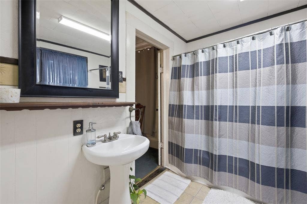 2309 Jones Street, Greenville, TX 75401 White pedestal sink with a dual-handle faucet, wall-mounted wood-finish shelf, and black-framed mirror