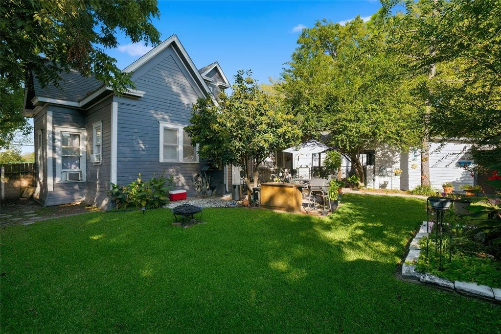 2309 Jones Street, Greenville, TX 75401 Backyard featuring lap siding, manicured lawn, mature trees, and stone-bordered garden beds