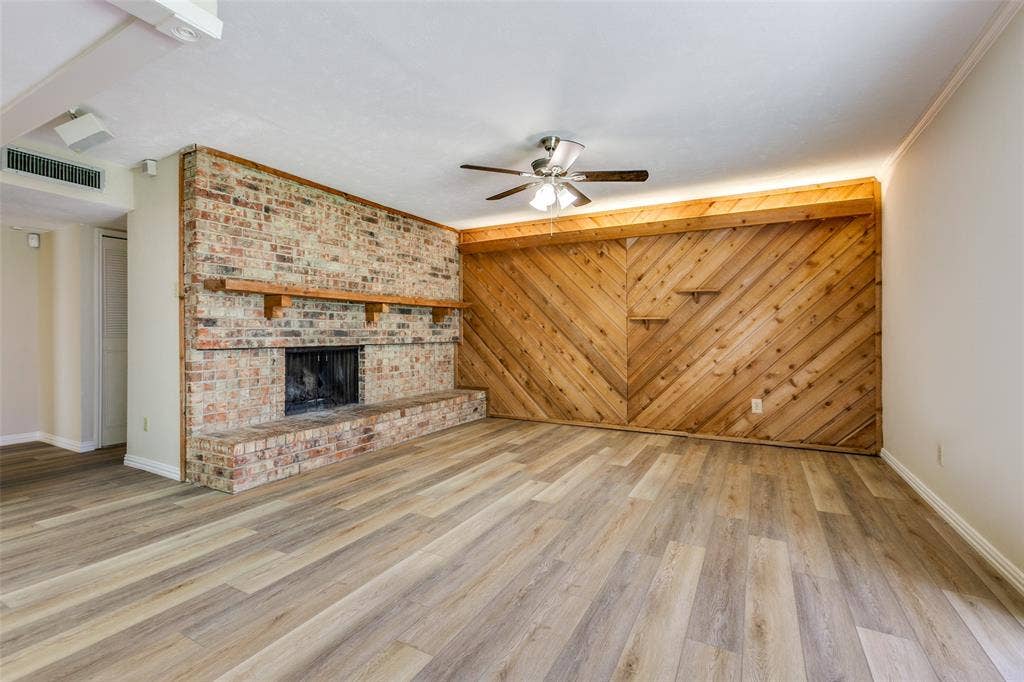 929 Arbor Downs Drive, Plano, TX 75023 Full-height brick fireplace featuring a wood mantel, diagonal wood-paneled accent wall with integrated shelving, and wood-finish flooring