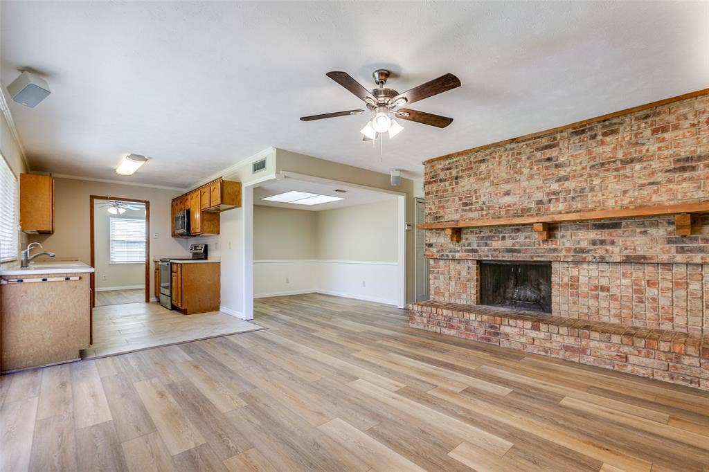 929 Arbor Downs Drive, Plano, TX 75023 Living area featuring wood-finish flooring, a floor-to-ceiling brick hearth, a wooden fireplace mantel, and a ceiling fan with integrated lighting
