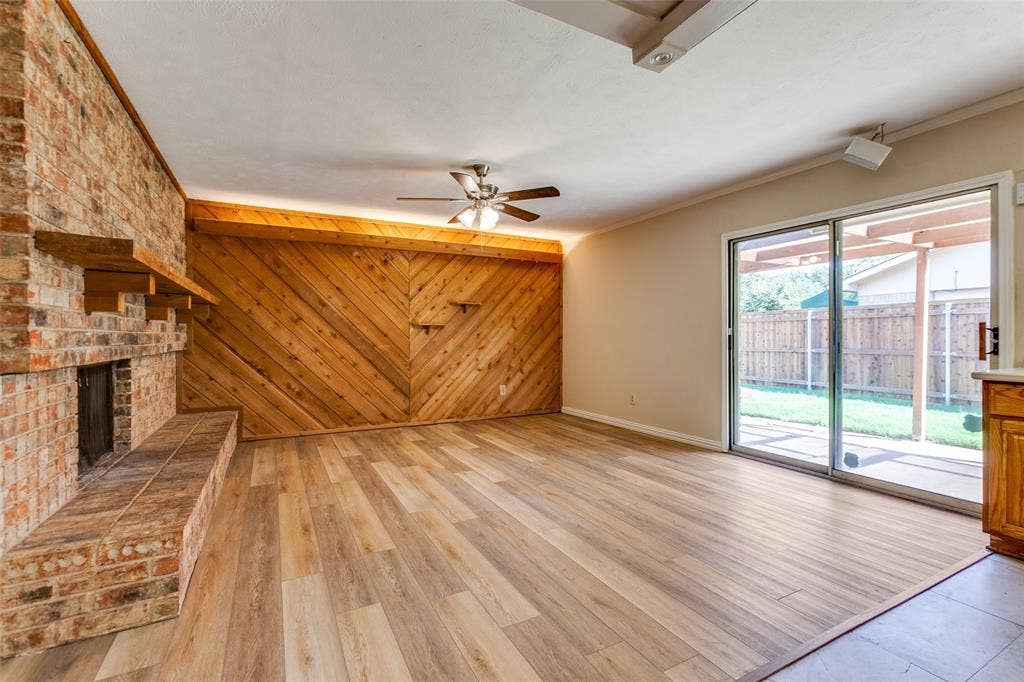929 Arbor Downs Drive, Plano, TX 75023 Living space featuring wood-finish flooring, a floor-to-ceiling brick fireplace with a wood mantel, diagonal wood-panel wall accents, a ceiling fan with integrated lighting, and sliding glass doors