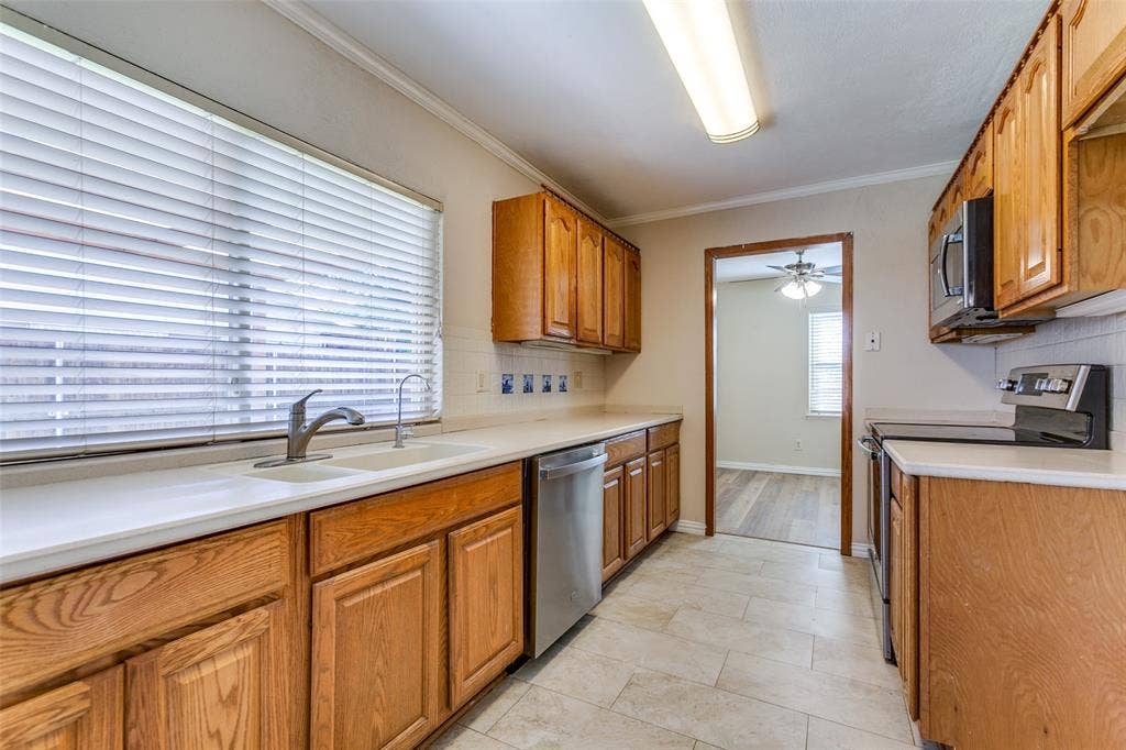 929 Arbor Downs Drive, Plano, TX 75023 Kitchen featuring natural wood cabinetry, white countertops, a dual-basin sink with a gooseneck faucet, stainless steel dishwasher, and tiled flooring