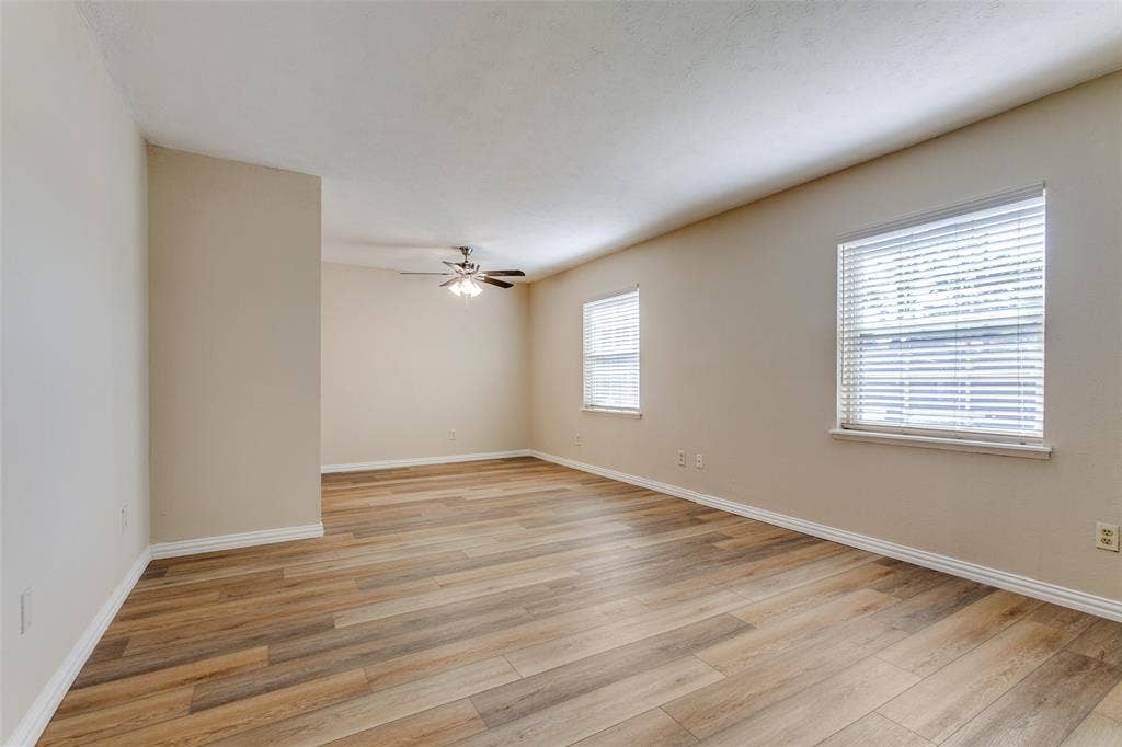 929 Arbor Downs Drive, Plano, TX 75023 Wood-finish flooring, neutral wall tones, two windows with horizontal blinds, and a multi-blade ceiling fan with integrated lighting