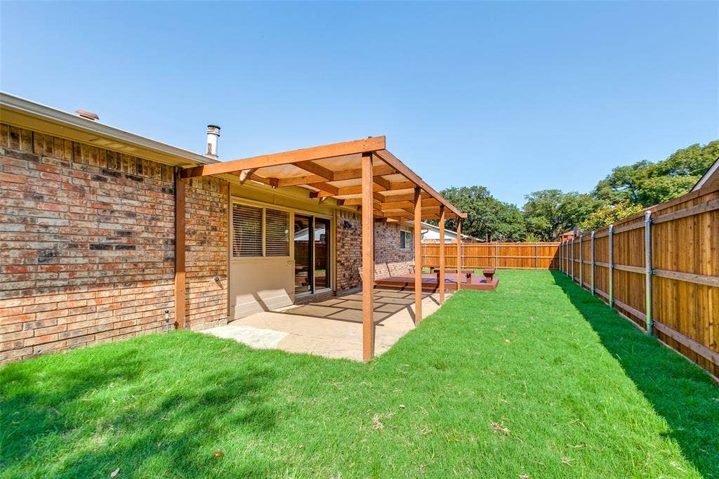 929 Arbor Downs Drive, Plano, TX 75023 Brick exterior, wood-framed pergola, concrete patio, and perimeter wood fencing