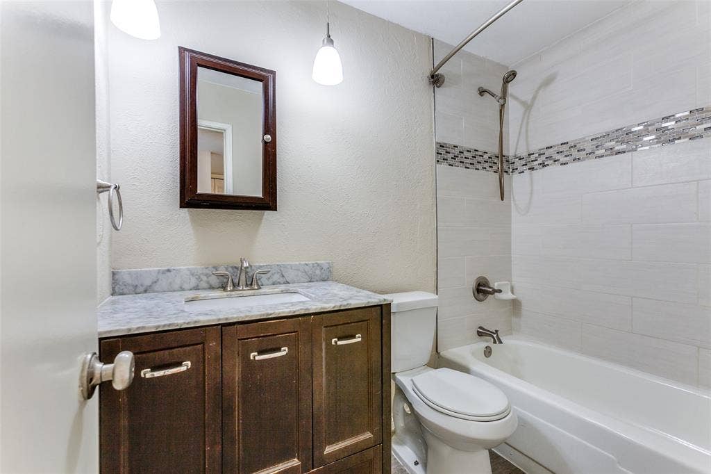 929 Arbor Downs Drive, Plano, TX 75023 Bathroom featuring a vanity with stone countertop, drop-in sink, dark wood cabinetry, and a shower-tub combination with decorative tile inlay