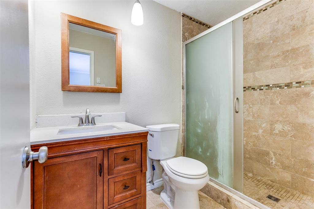 929 Arbor Downs Drive, Plano, TX 75023 Bathroom vanity with wood-finish cabinetry, inset sink, framed wall mirror, and shower stall with tile surround and decorative stone-tile accent band