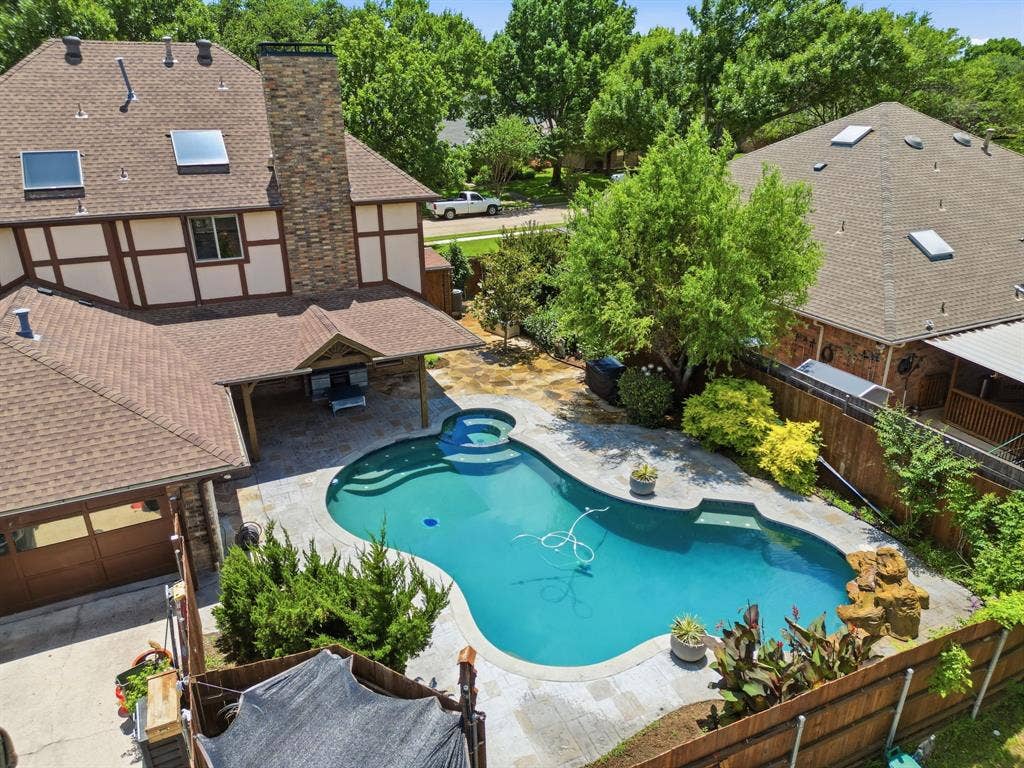 1509 Aylesbury Lane, Plano, TX 75075 Backyard featuring an in-ground swimming pool with an integrated spa, stone masonry chimney, covered patio, and wood-finish garage door