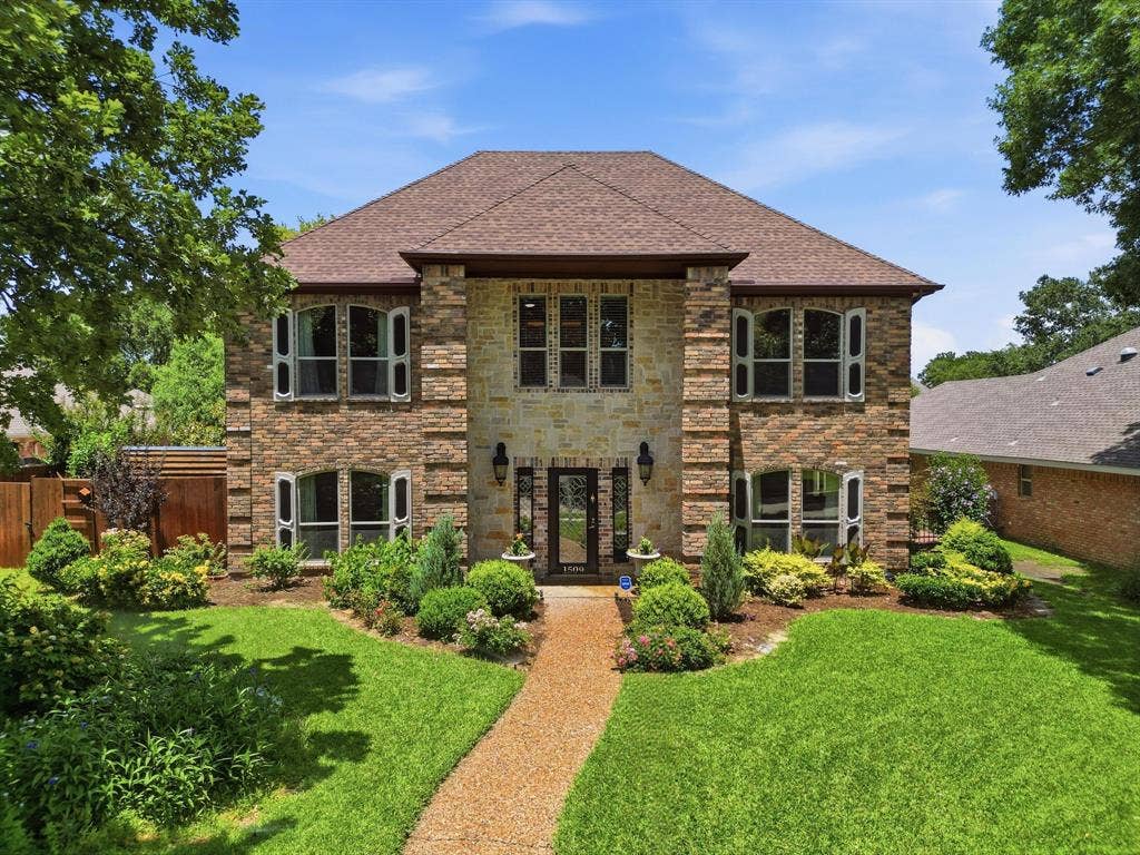 1509 Aylesbury Lane, Plano, TX 75075 Two-story exterior featuring multi-toned brick and stone masonry, hip roof, arched window detailing, and a stone-paved walkway