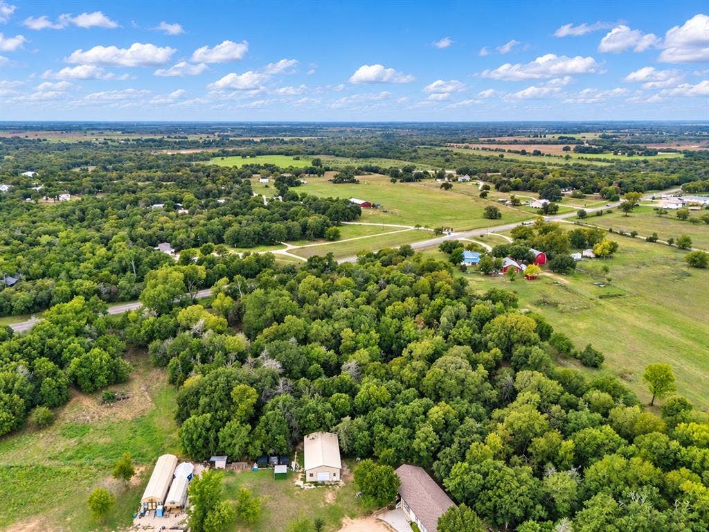 Aerial perspective of expansive acreage featuring mature tree clusters, open pasture land, and detached metal outbuildings