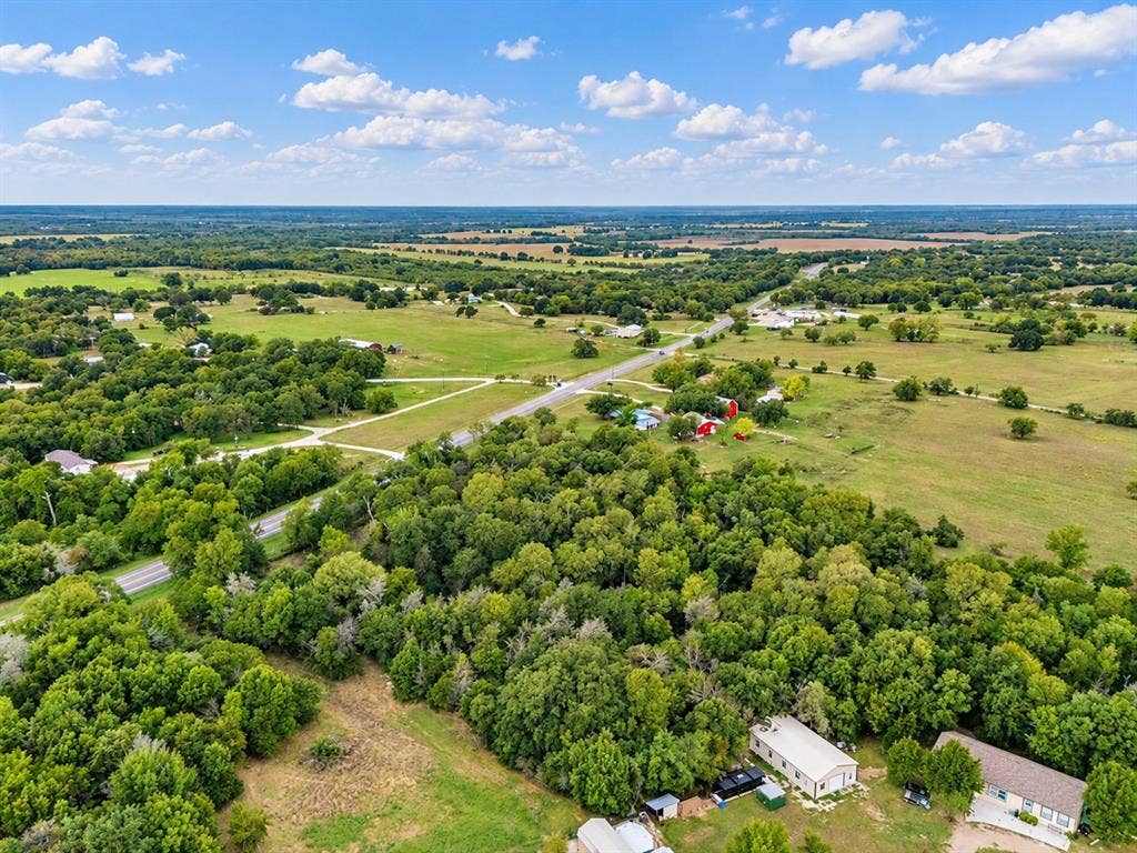 Aerial view of expansive acreage featuring mature hardwood trees, open pastureland, and multiple outbuildings