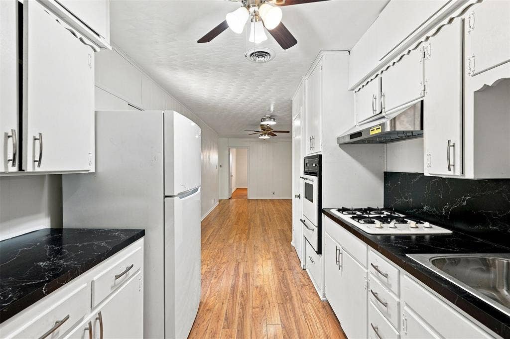 Kitchen featuring white cabinetry with silver-tone hardware, dark marbled countertops, and a stainless steel sink