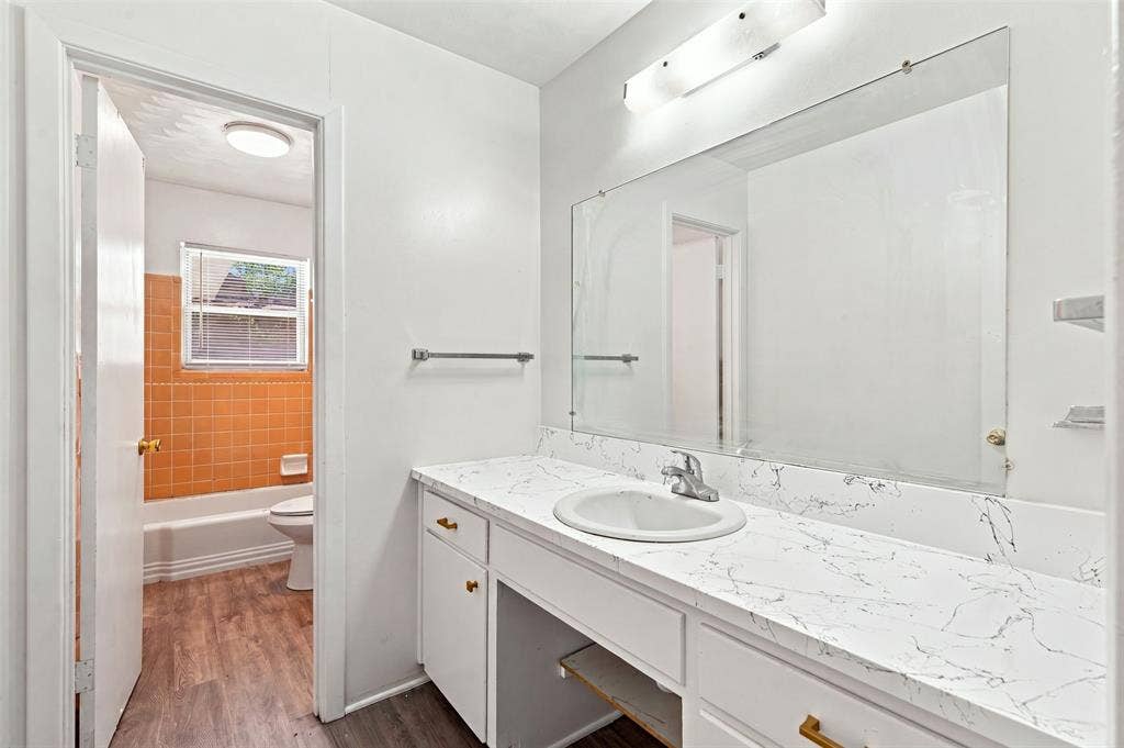 Vanity featuring a white countertop with integrated sink, white cabinetry with gold-finish hardware, and a large wall-mounted mirror