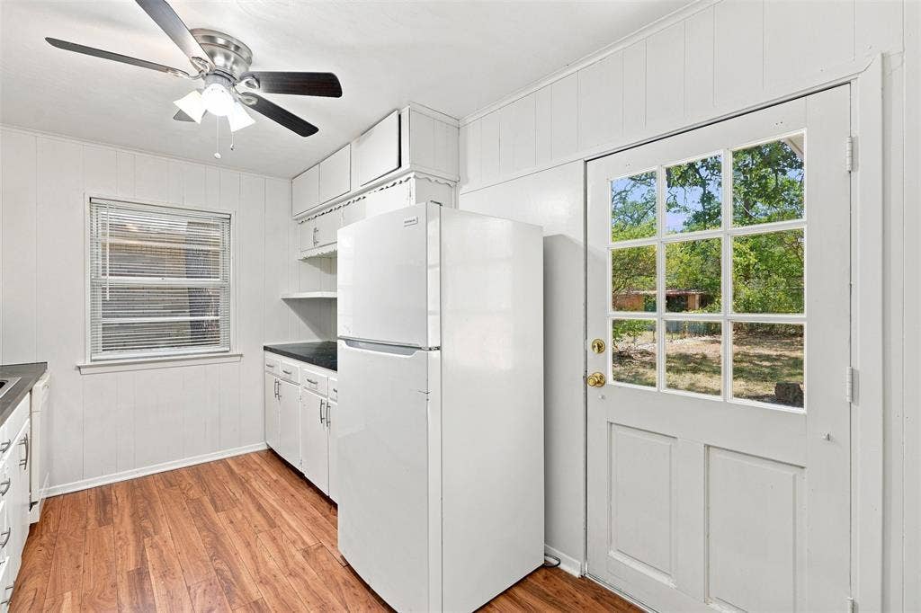 Kitchen area featuring wood-finish flooring, white cabinetry, dark countertops, and a ceiling fan with light fixture