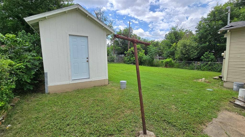 922 Hollywood Avenue, Dallas, TX 75208 Backyard featuring a standalone storage structure with vertical siding, a paved concrete foundation, and a perimeter chain-link fence