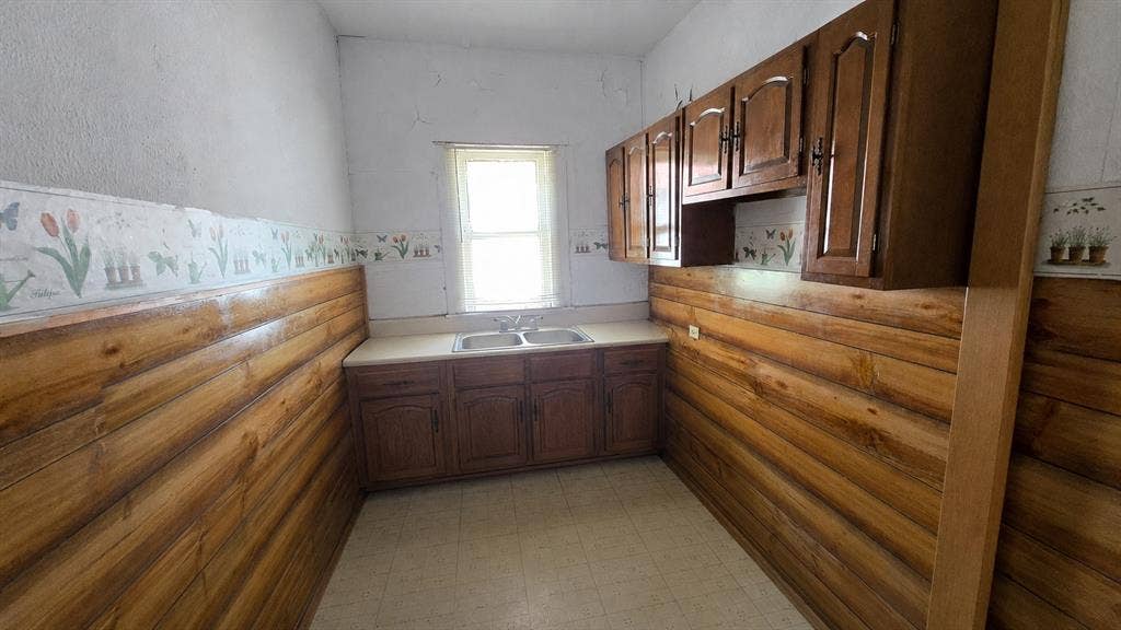 922 Hollywood Avenue, Dallas, TX 75208 Kitchen featuring wood-paneled walls, built-in upper and lower wood cabinetry, solid-surface countertop, double-basin sink with dual-handle faucet, and tile flooring