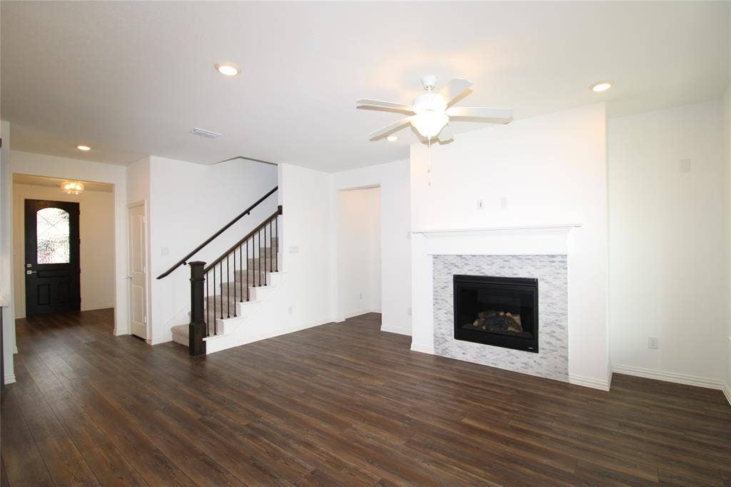 2603 Swallowtail Street, Melissa, TX 75454 Wood-finish flooring, fireplace with stone-patterned tile surround, fireplace mantel, ceiling fan, and staircase with wooden handrail and balusters