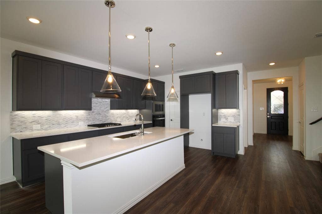 2603 Swallowtail Street, Melissa, TX 75454 Kitchen featuring dark shaker-style cabinetry, quartz countertops, a central island with a sink, glass pendant lighting, and wood-finish flooring