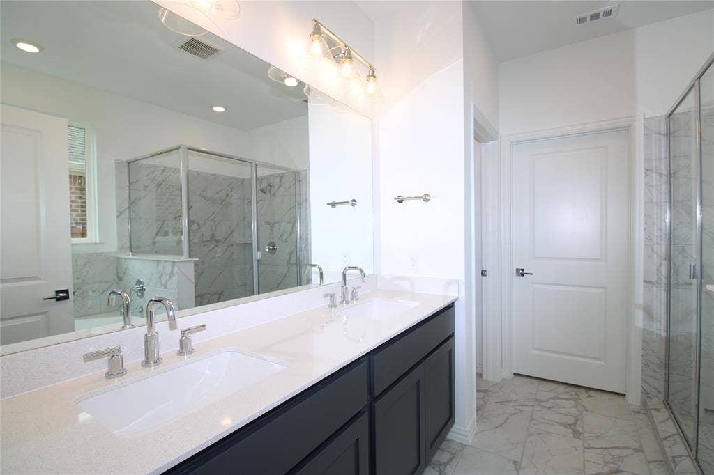 2603 Swallowtail Street, Melissa, TX 75454 Dual-sink vanity with white countertops, dark cabinetry, polished metal fixtures, full-width mirror, and stone-finish floor tiling