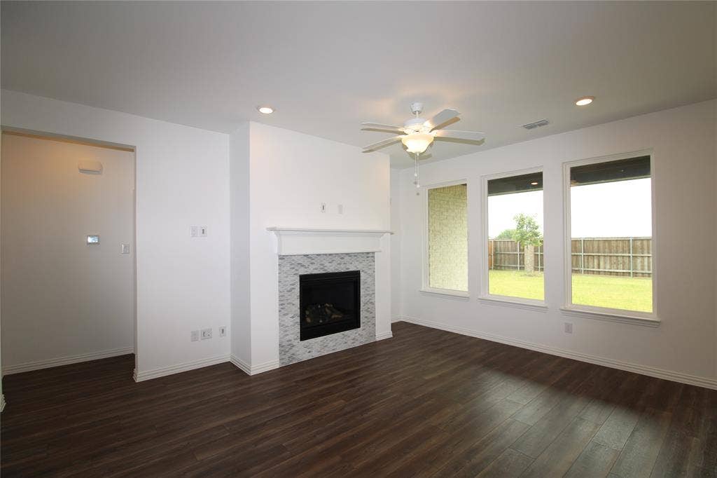 2603 Swallowtail Street, Melissa, TX 75454 Living area featuring wood-finish flooring, a fireplace with decorative tile surround and a crown-molded mantel, three large windows, and a ceiling fan with integrated lighting