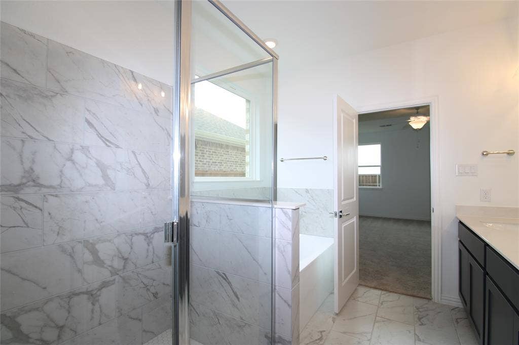 2603 Swallowtail Street, Melissa, TX 75454 Bathroom featuring a walk-in shower with large-format tile surround, a built-in soaking tub, a dark-finish vanity with a solid-surface countertop, and patterned stone-finish floor tiling